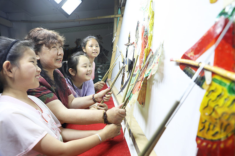 皮影藝人指導(dǎo)小朋友表演皮影戲。